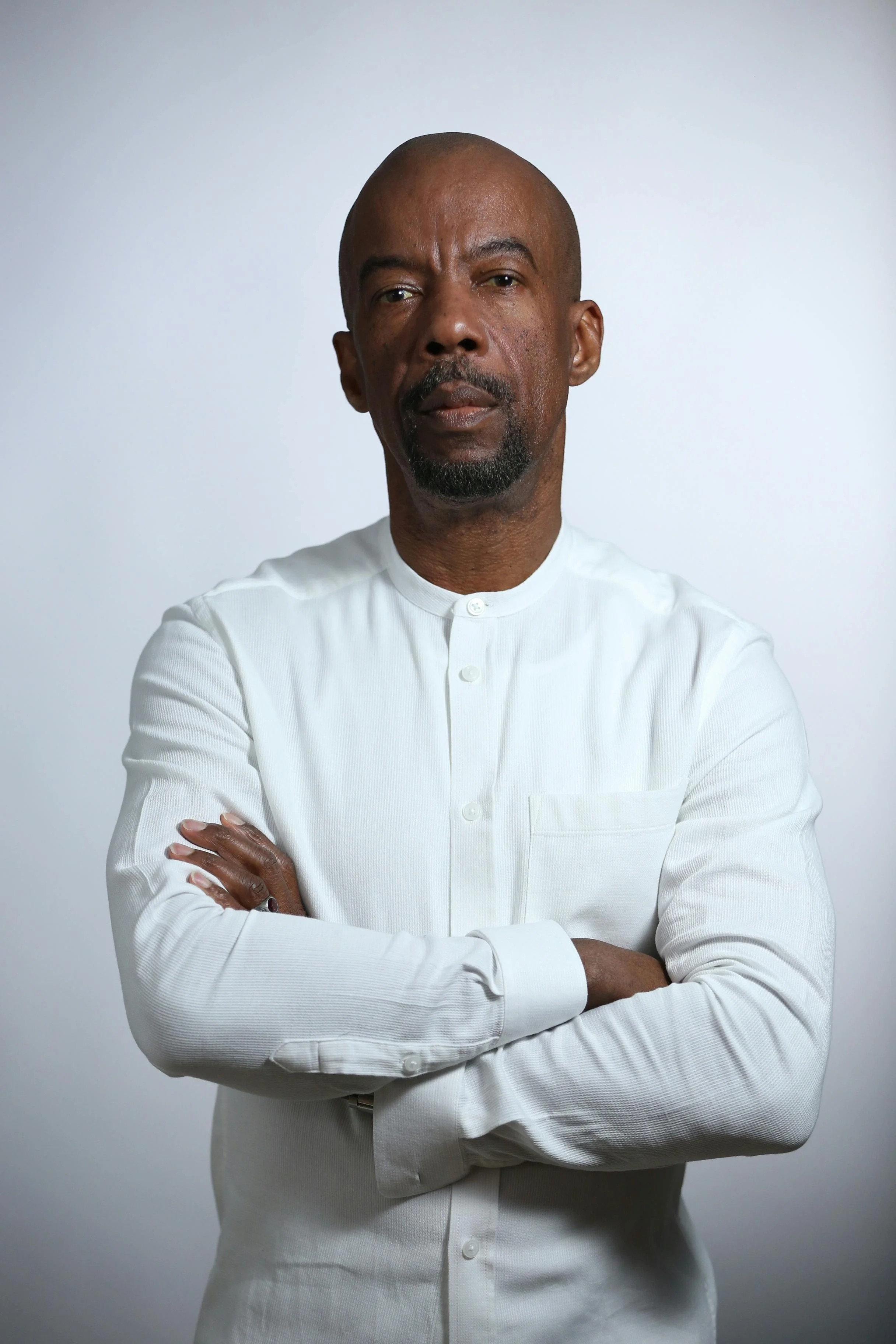 Photoreal digital twin of a man with short dark hair wearing a crisp white button-down shirt and light gray trousers on a pale steel-blue background.